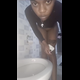 A slim black woman in a black top bends over a toilet and spreads her oiled cheeks for the camera. A soft turd slowly peeks out of her ass, followed by a pee stream. She wipes at the end. No product reveal. Vertical format video. About a minute.